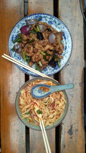 two plates of food on a wooden table with chopsticks at Pingyao Jiaxin Guesthouse in Pingyao