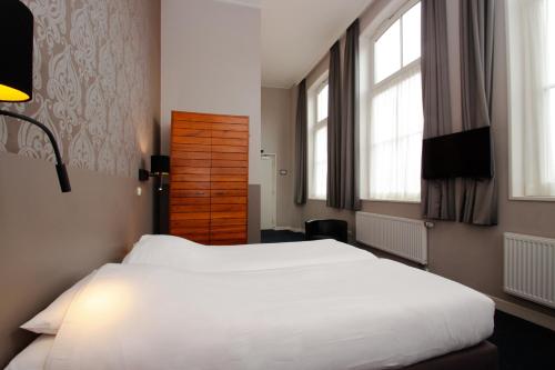 a large white bed in a room with windows at Hotel Aan De Singel in Delfzijl