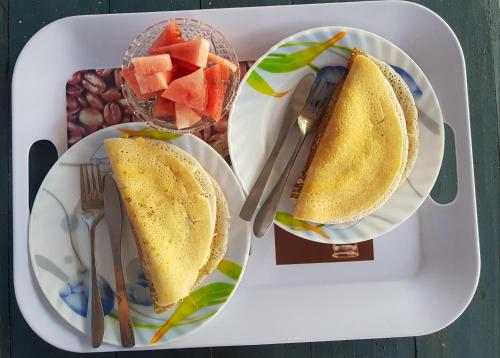 a tray with two sandwiches and a bowl of fruit at Nilaveli Beach Rooms in Nilaveli