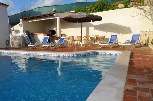 een zwembad met blauwe stoelen en een parasol bij Casa do Poco in Armação de Pêra