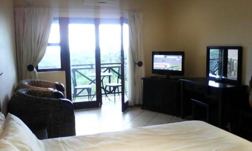 Un dormitorio con una cama y un televisor y un balcón. en Ocean View Villas C11, en Port Edward