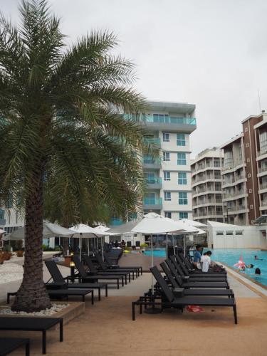a row of chairs and a palm tree next to a pool at Grand Blue Condominium by Mary in Mae Pim