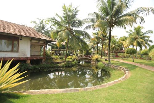 a house with a pond in a yard with palm trees at Kalathil Lake Resort in Vaikom