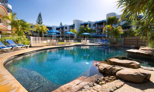 a swimming pool in a resort with chairs and umbrellas at Headland Tropicana Resort in Alexandra Headland