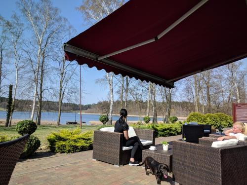 two people sitting on chairs under awning with a dog at Villa Plena in Ośno Lubuskie