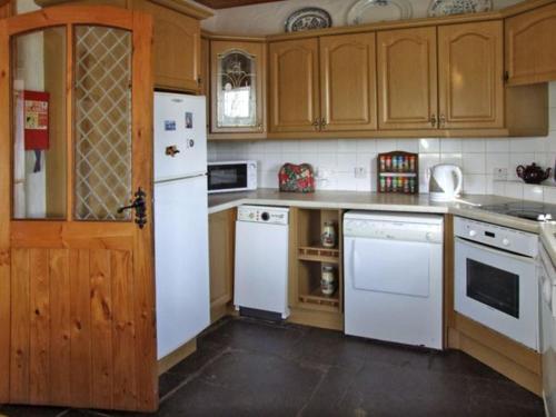 una cocina con electrodomésticos blancos y armarios de madera en Delia's Cottage, en Ballinrobe