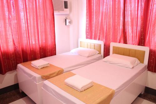 two beds in a room with red curtains at Butuan Grand Palace Hotel Annex in Butuan