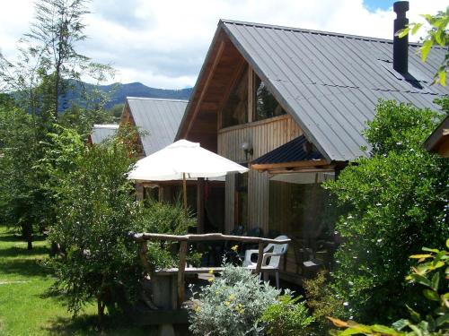 a house with a table and an umbrella in the yard at Hosteria-Cabañas Rucapillan in Choshuenco