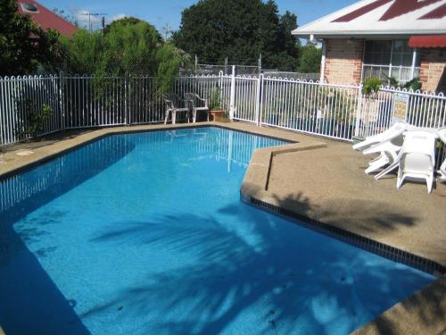 una piscina con 2 sillas blancas y una valla en Beenleigh Village Motel, en Beenleigh