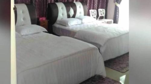two beds in a hotel room with white sheets at Paka Tamim Seaview Hotel in Paka