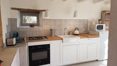 a kitchen with white cabinets and a sink and a microwave at Le Clos Des Etoiles in Le Bugue