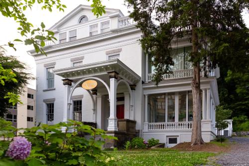 a white house with a porch and a tree at Argos Inn - Ithaca's Boutique Hotel in Ithaca