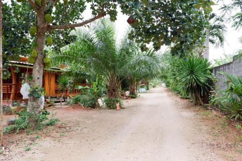 a dirt road in front of a house with palm trees at Baansuan Resort in Don Sak