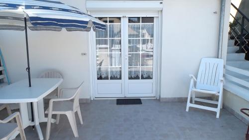 een patio met een tafel en stoelen en een parasol bij La Caravelle 10 Boulevard Gilbert Longuet in Arromanches-les-Bains