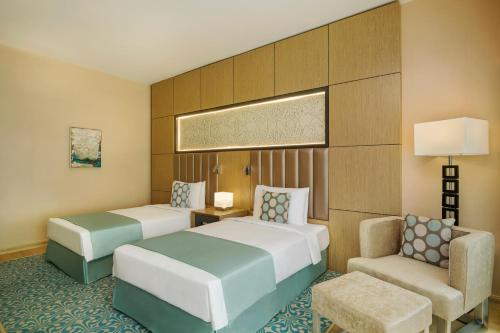a hotel room with two beds and a chair at Wyndham Doha West Bay in Doha