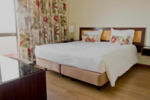 a bedroom with a large white bed with floral curtains at Hotel D. Luis in Coimbra