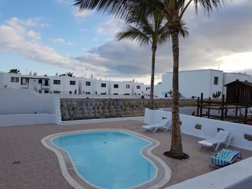 - une piscine bordée de palmiers et de bâtiments blancs dans l'établissement Apartmento Juana 2, à Puerto del Carmen