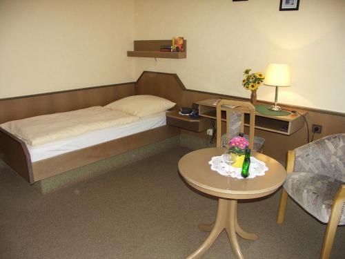 Habitación pequeña con cama y mesa con flores. en Pension Wölfel, en Bad Steben