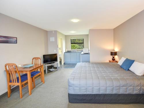 a bedroom with a bed and a table and a kitchen at Bonnie Knights Motel Mosgiel in Mosgiel