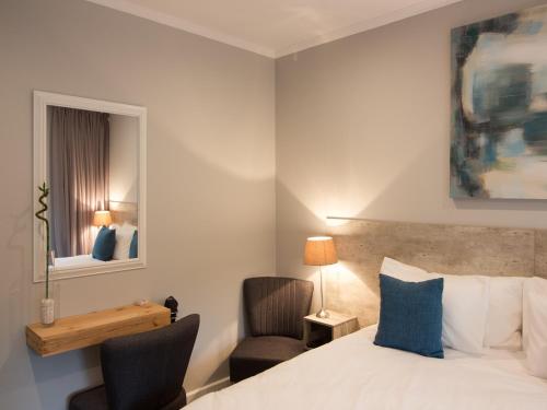 a bedroom with a bed and a chair and a mirror at The Greens Guest House in Knysna