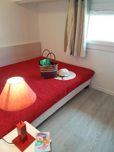 Habitación con cama roja con lámpara y cesta en Résidence Goélia Sun Village, en Portiragnes