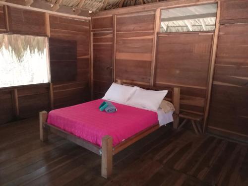 Cama pequeña en habitación con manta rosa en Cabanas Las Estrellas en Palomino