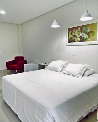 a bedroom with a white bed and a red chair at Hotel Picadão in São Pedro