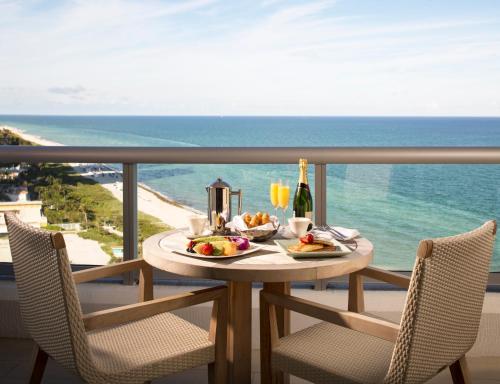 ein Tisch mit Essen und Wein auf einem Balkon mit Blick auf das Meer in der Unterkunft Eden Roc Miami Beach in Miami Beach