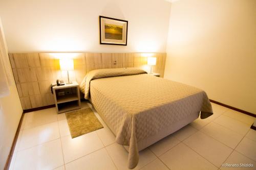 a bedroom with a bed and a nightstand with two lamps at Aruá Hotel, Restaurante e Convenções in Presidente Prudente