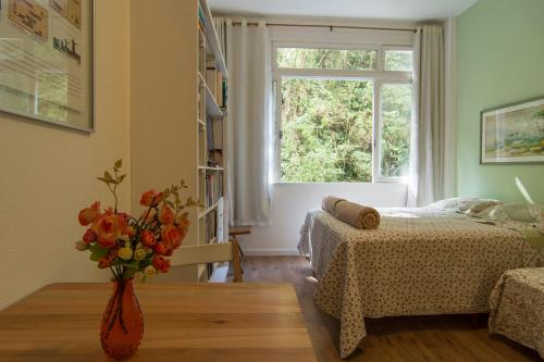 1 dormitorio con 1 cama y un jarrón de flores sobre una mesa en Flat 407, en Petrópolis