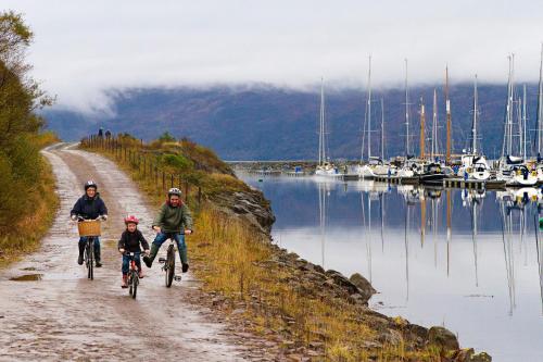 three people riding bikes down a dirt road next to a marina at Portavadie Loch Fyne Scotland in Portavadie