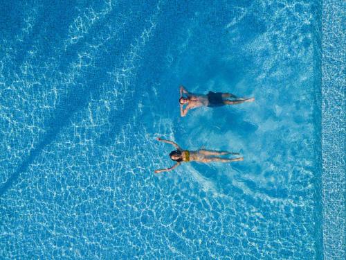 two people swimming in a pool of blue water at Dhigali Maldives - A Premium All-Inclusive Resort in Raa Atoll