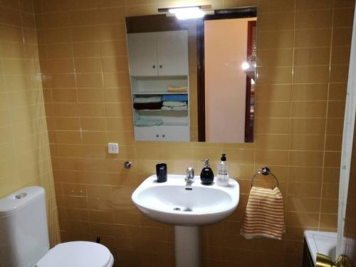een badkamer met een wastafel, een toilet en een spiegel bij Atico primer linea de mar con piscina en EbreHogar in Sant Carles de la Ràpita