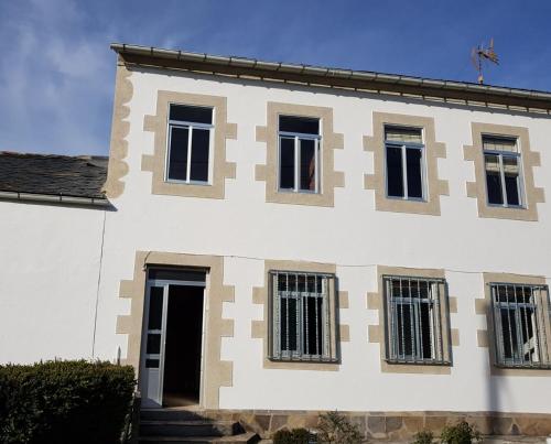a white building with black windows and a door at Casa de Campo Cruz de Pedra in Portomarin