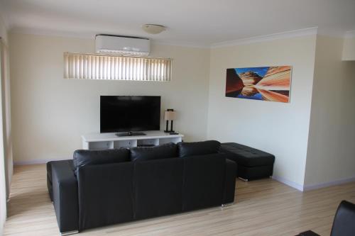 a living room with a black couch and a flat screen tv at Seaspray Beach Holiday Park in Dongara