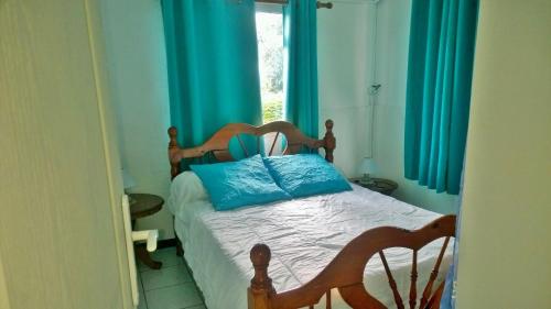 a bedroom with a bed with blue curtains and a window at Les Bungalows du Mont-Auban in Sainte-Clotilde