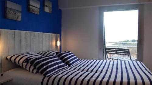 een slaapkamer met een bed met gestreepte kussens en een raam bij Kerwelmor, appartement avec vue sur la mer in Saint-Quay-Portrieux