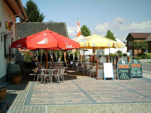 un patio con mesas, sillas y sombrillas en gasthof lederhose en Diepenbeek