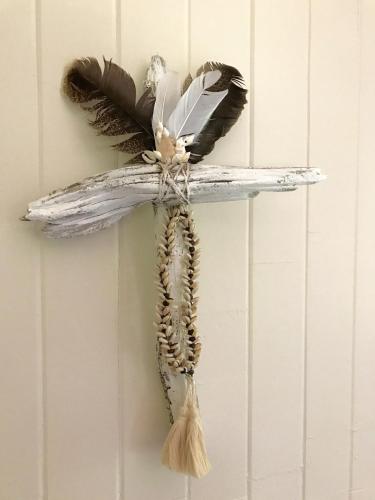 a cross hanging on a wall with feathers on it at Daintree Magic Holiday House in Cow Bay