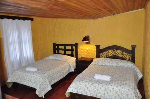 two beds in a room with yellow walls at Hotel Museo la Posada del Molino in El Cocuy