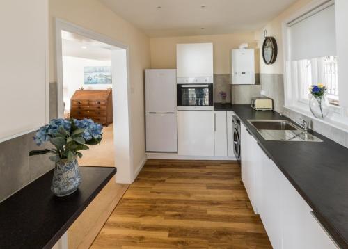 a kitchen with white appliances and a vase of flowers on the counter at Beachside Apartment, 1 Pilots Point in Totland