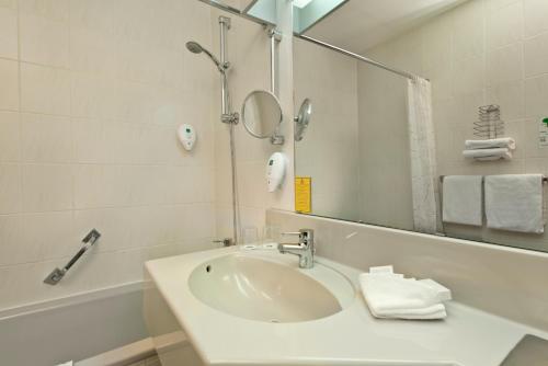 ein weißes Badezimmer mit einem Waschbecken und einem Spiegel in der Unterkunft Wyndham Garden Kassel in Kassel