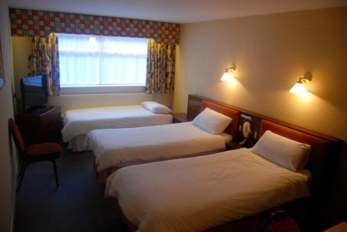 a hotel room with three beds and a window at Brecon Hotel Sheffield Rotherham in Rotherham