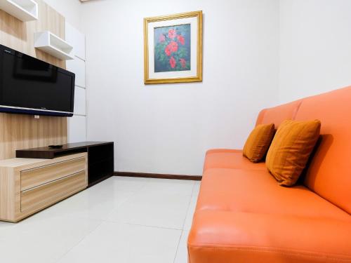 a living room with an orange couch and a flat screen tv at Homey 1 BR Apartment Thamrin Residence By Travelio in Jakarta