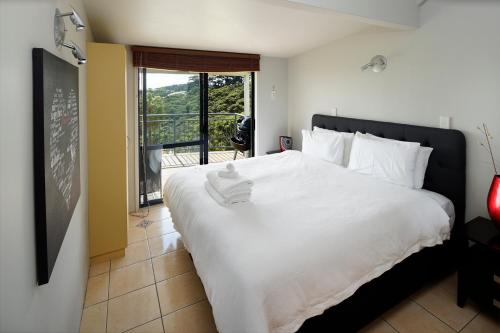 a bedroom with a large white bed and a balcony at Palm Waiheke Island Resort in Palm Beach