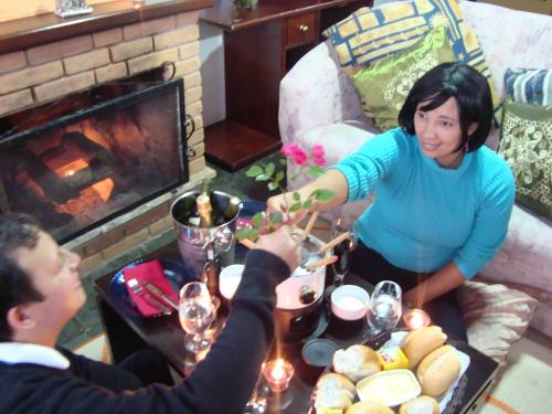 a man and a woman preparing a table in front of a fireplace at Chalé Suiço de Campos do Jordão in Campos do Jordão