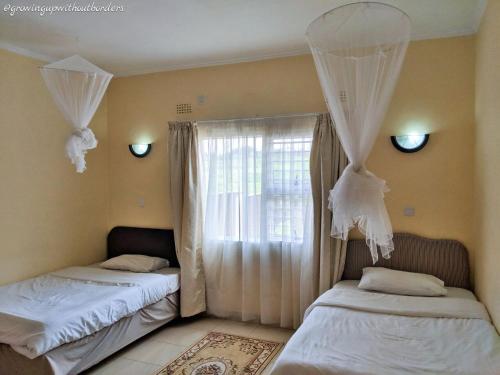 Un dormitorio con dos camas y una ventana con cortinas. en Home Up Guest Apartments and Lodge, en Blantyre