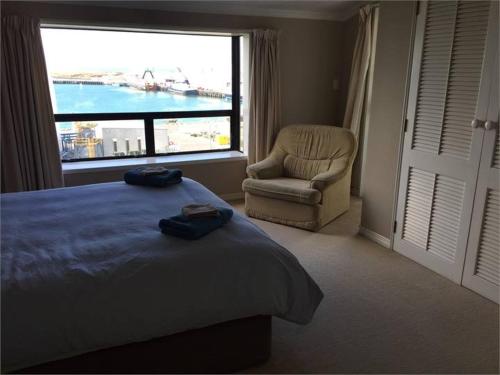 a bedroom with a bed and a chair and a window at Terrace Apartment in Timaru