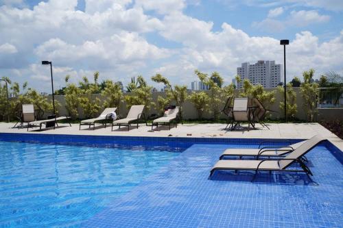 a swimming pool with chaise lounges and chairs on a building at Conforto no Alto da Boa Vista in São Paulo
