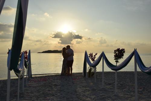 a couple standing on the beach with the sun in the background at Araamu Hotels Maldives at Dhiffushi in Dhiffushi